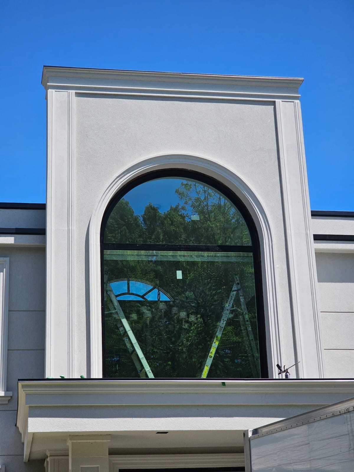 Close-up of the custom radius-top arched window with slim black frame over the porch roof