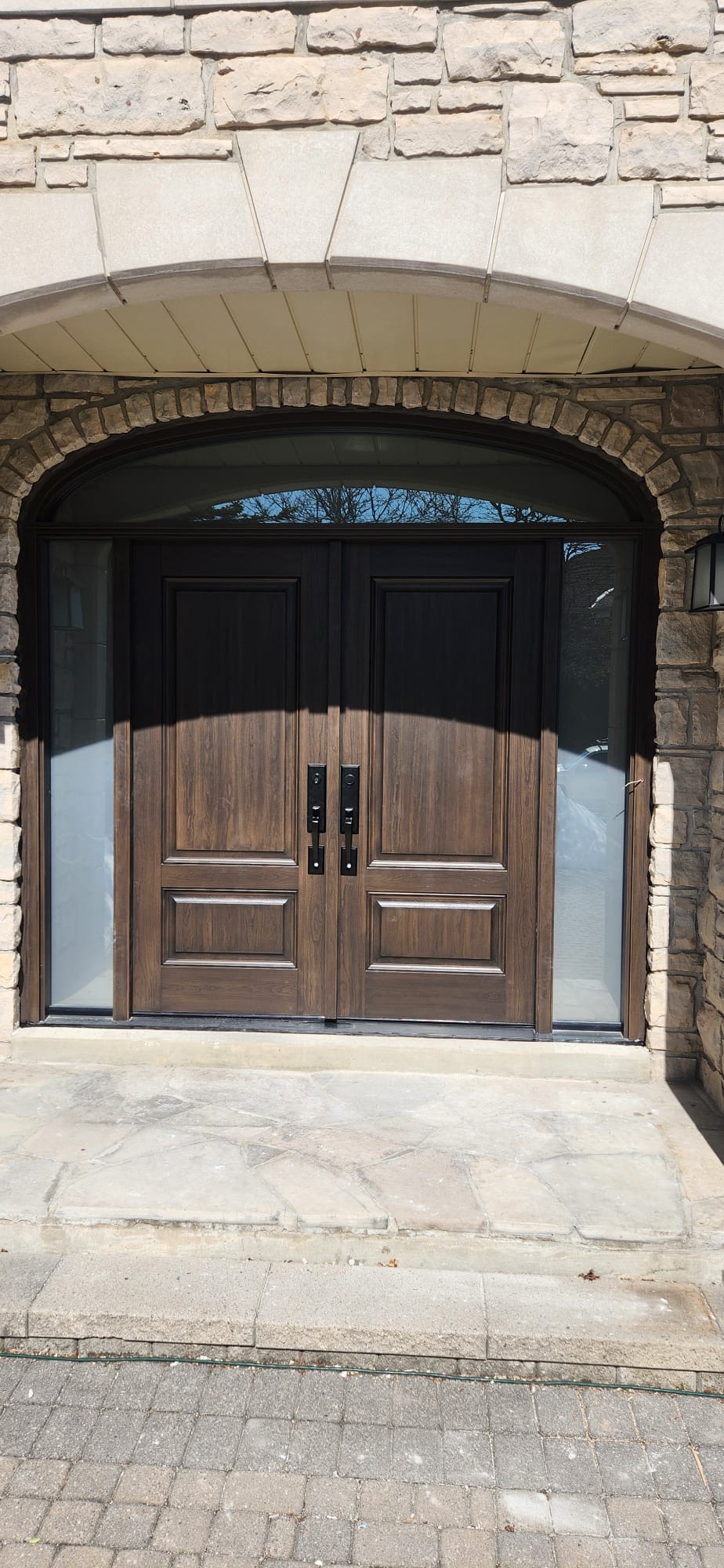 Walnut fiberglass double entry doors under an arched stone surround