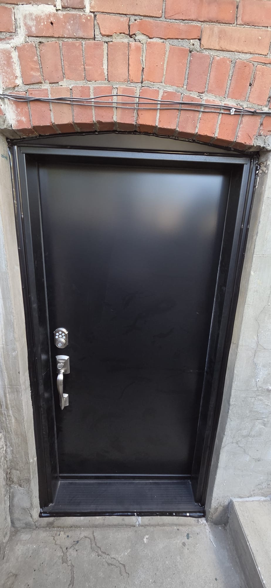 Matte black steel basement entry door on brick foundation