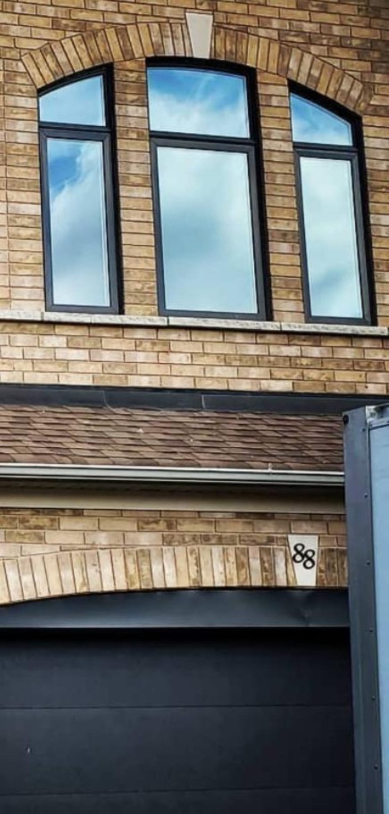 Trio of custom arch-top black windows above a garage elevation